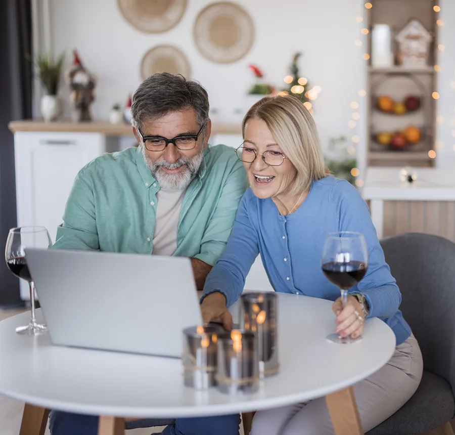 couple in their 50s sitting at dining table drinking wine and looking at laptop together